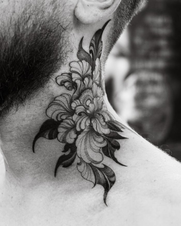 Detailed close-up of a floral tattoo on a man's neck in black and white.