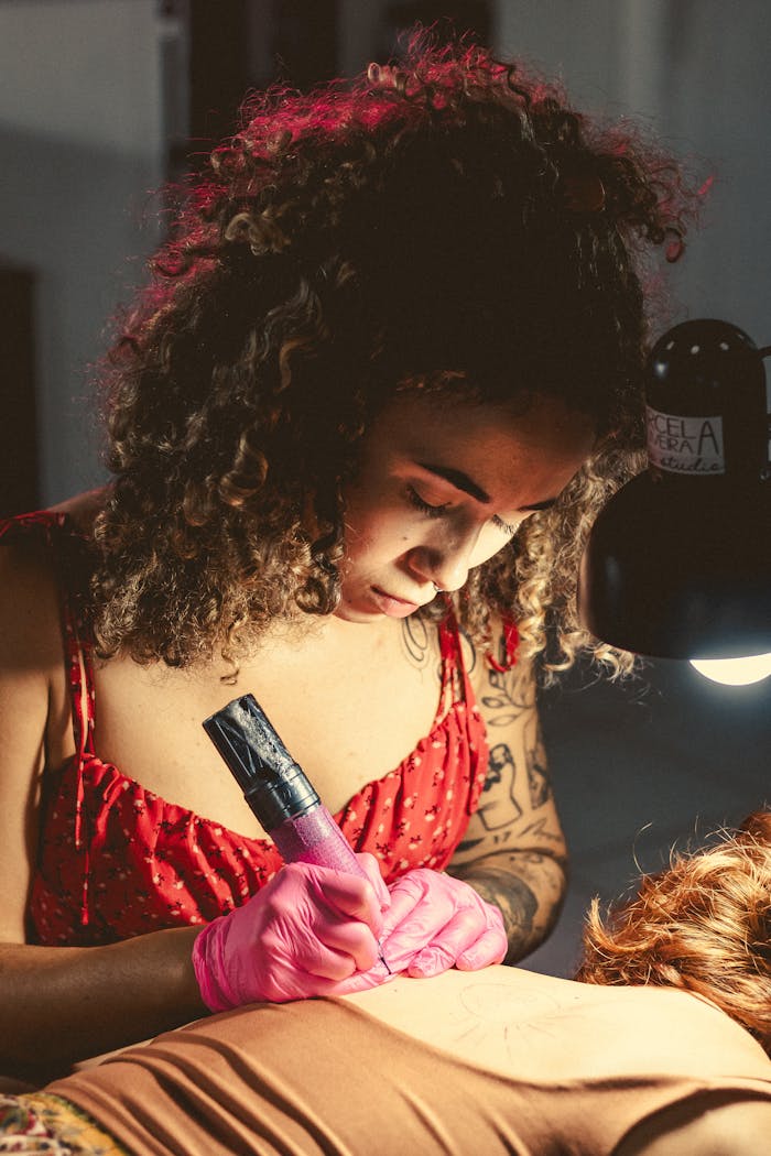 Young female tattoo artist meticulously working on a client's tattoo indoors.