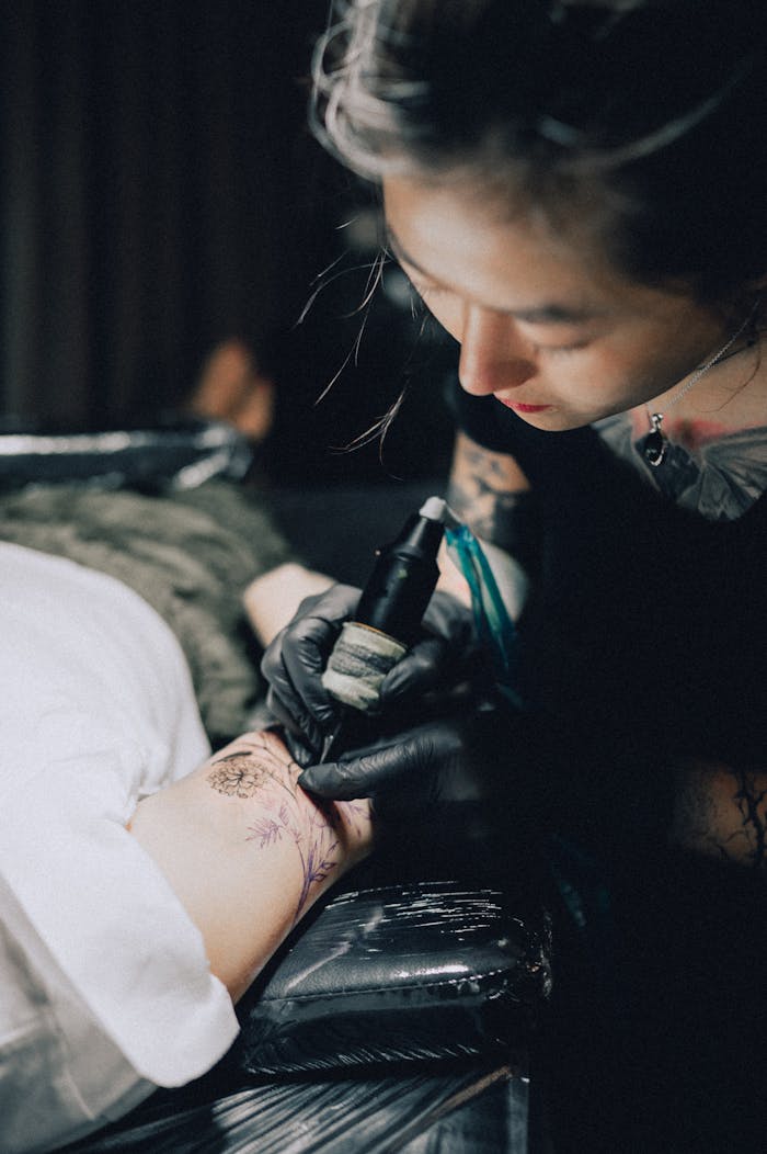 A skilled tattoo artist creates intricate designs on a client's arm indoors.